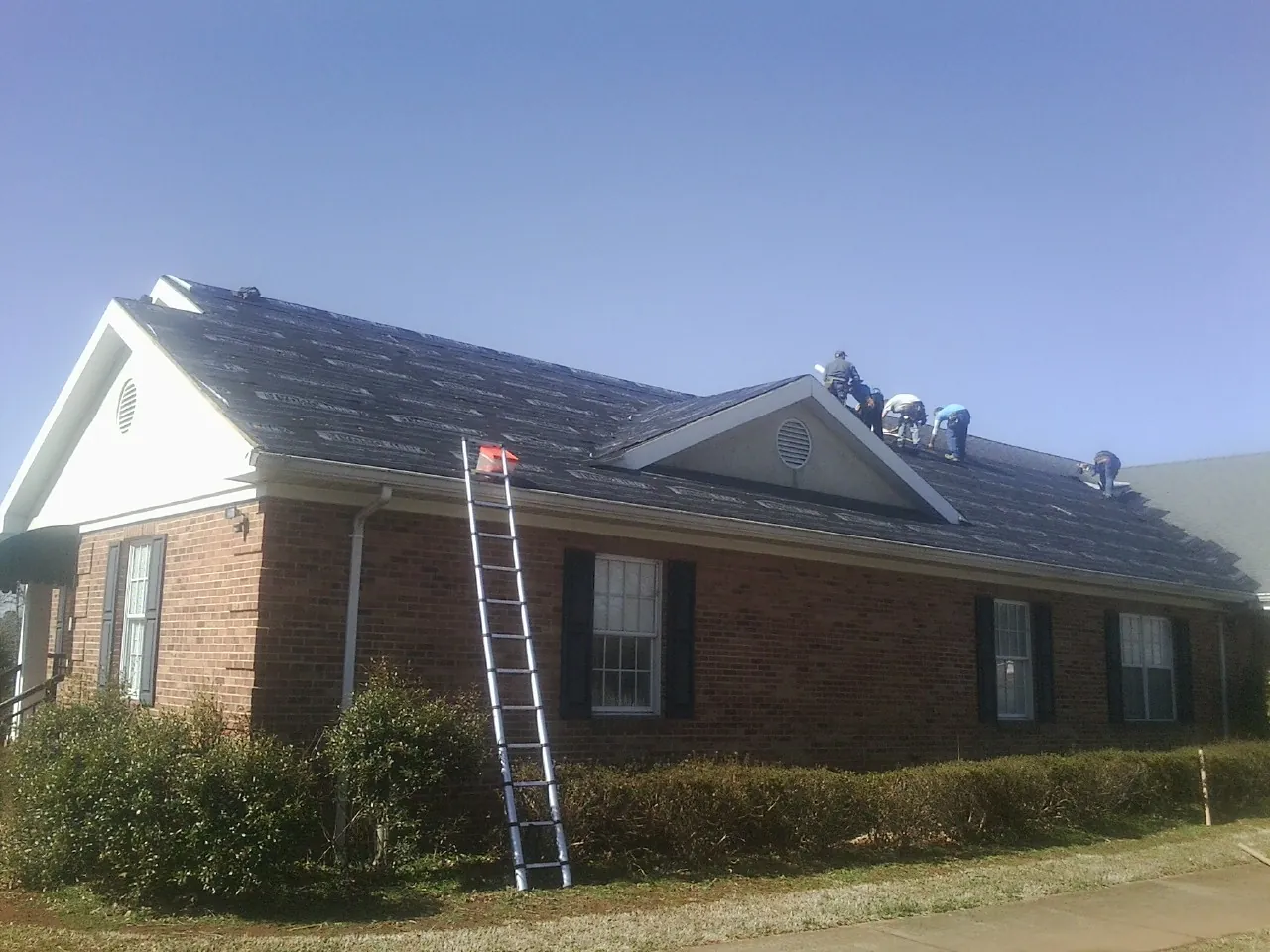 Crew tearing shingles off a brick ranch roof with a ladder set — Emergency Roof Repair work by our crew in San Ramon