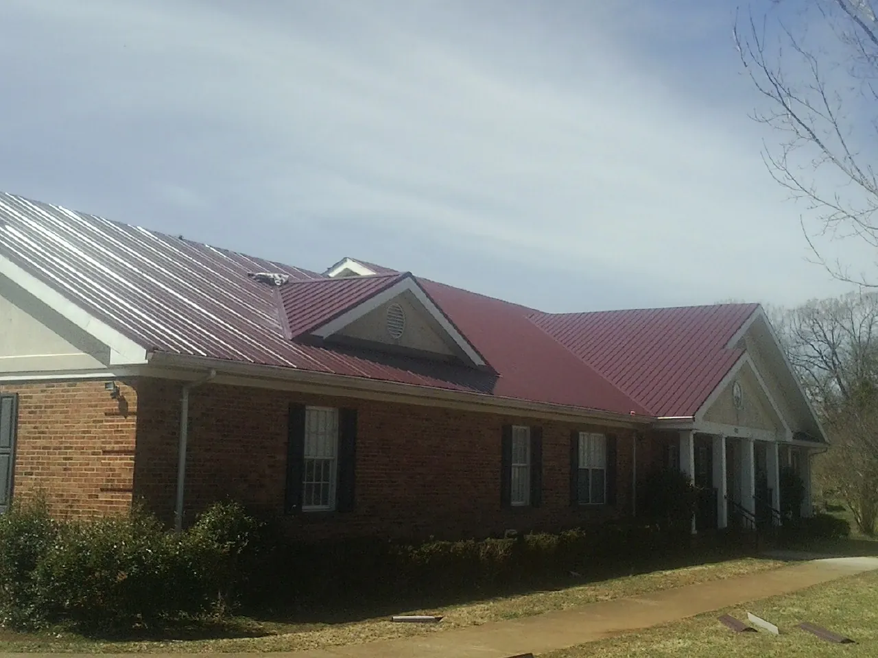 Red metal roof with gabled entries on a long brick building, from a Hail Damage Roof Repair job in San Ramon