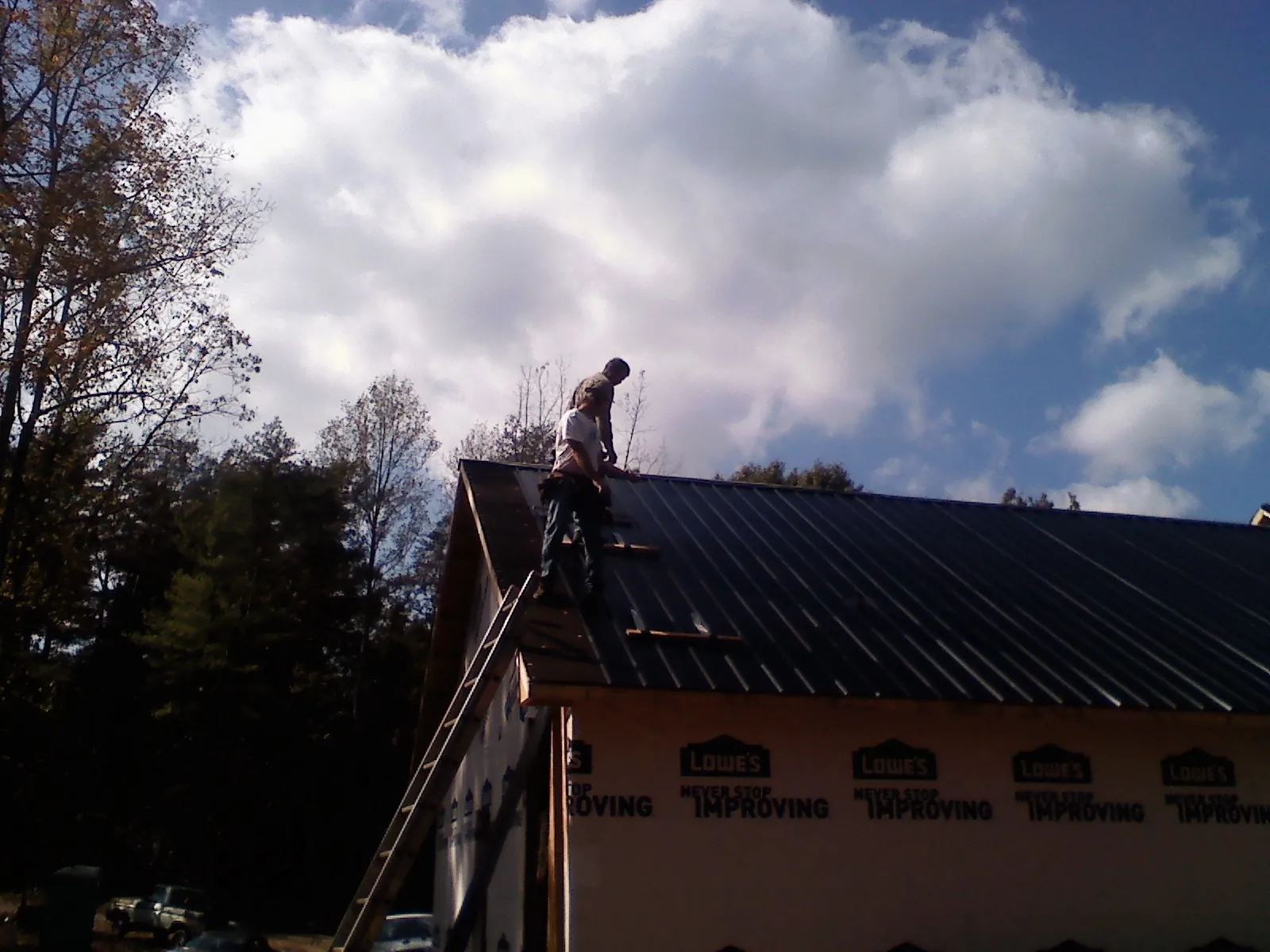 Roofer fastening dark metal panels high against a cloudy sky, from a Roof Inspection job in San Ramon